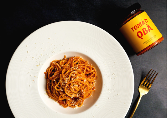 TOMÁTÌ ỌBÀ spaghetti on a white plate with grated Parmesan and a gold fork